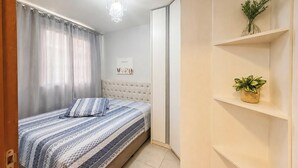 A bedroom with a bed, a chandelier, a framed picture, a plant, and a wardrobe. - Nautilus Ap Vista Mar (Penha)