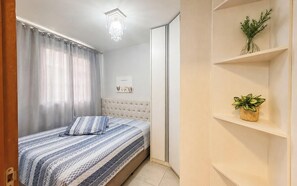 A bedroom with a bed, a chandelier, a framed picture, a plant, and a wardrobe. - Nautilus Ap Vista Mar (Penha)
