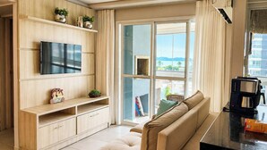 A modern living room with a flat-screen TV, wooden cabinetry, a sofa, and a coffee machine. - Nautilus Ap Vista Mar (Penha)