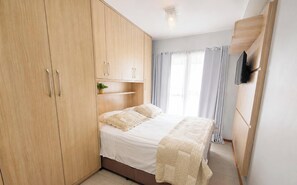 Un dormitorio con una cama, un armario de madera y un televisor montado en la pared.