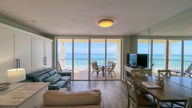 Un salon avec un canapé, une table à manger et un téléviseur. Il y a un balcon avec vue sur la plage.