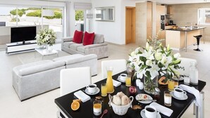 A modern hotel room with a dining area, a sofa, a TV, and a kitchen area. - Praia del Rey 3 Bedroom Villa (Obidos)