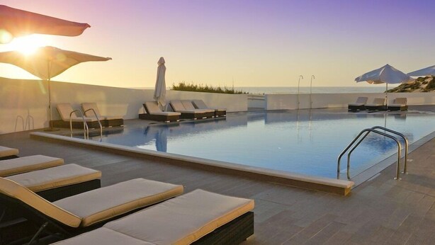 A rooftop pool with lounge chairs and umbrellas, overlooking a body of water. - Praia del Rey 3 Bedroom Villa (Obidos)