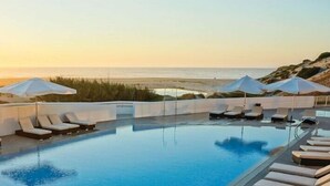 A rooftop infinity pool with lounge chairs and umbrellas, overlooking a beach at sunset. - Praia del Rey 3 Bedroom Villa (Obidos)