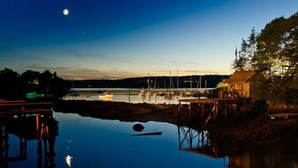 A marina at dusk with boats docked, a wooden pier, and a small building.