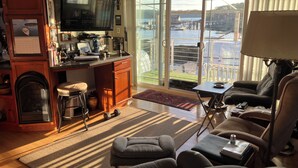 A living room with a fireplace, a television, a sofa, and a view of a dock and water.