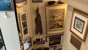 A staircase leading to a room with a wooden floor, a door with a brass handle, and a wall adorned with framed pictures and a plaque.