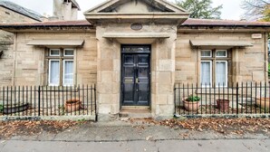 A stone building with a black door, two windows, and a triangular pediment. - GuestReady - Peaceful 2BR near Holyrood Park (Edinburgh)