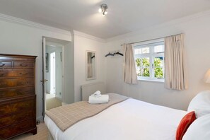 A bedroom with a bed, a dresser, a window with curtains, and a radiator.