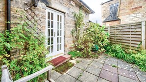 A stone building with a white door, a small garden with various plants, and a wooden fence. - GuestReady - Peaceful 2BR near Holyrood Park (Edinburgh)