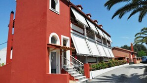 A red building with a white awning, a staircase, and a car parked nearby.