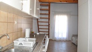 A compact kitchen with a built-in stove, a sink, and a wooden ladder leading to a small sleeping area.