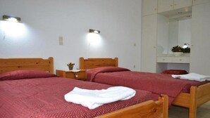A bedroom with two wooden beds, each with a red quilt and white towels. There are bedside tables with lamps and a mirror above the bed.