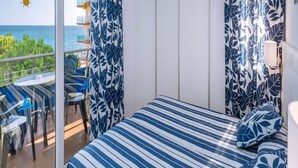 A balcony with a view of the sea, a bed with a striped bedspread, and blue and white patterned curtains. - Hotel Tahiti Playa and Suites (Santa Susanna)