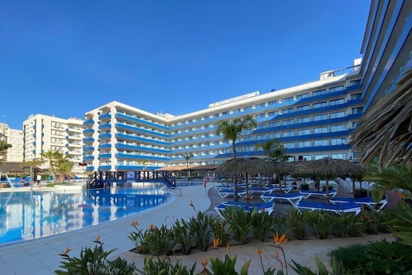 A hotel with a large pool area, multiple balconies, and a clear blue sky.