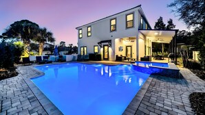 Ein modernes, zweistöckiges Haus mit Swimmingpool, Sitzgelegenheiten im Freien und einer überdachten Terrasse.