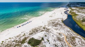 Vista aérea de una playa con aguas turquesas cristalinas, una orilla de arena y algunas sombrillas.