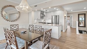 Una cocina moderna con armarios blancos, una isla central y un comedor con mesa de vidrio y sillas de mimbre.