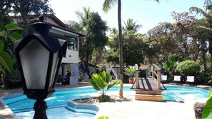 A pool area with a fountain, palm trees, and a building with a tiled roof. - Pousada Solar das Orquídeas Praia (Porto Seguro)