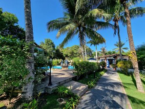 A tropical resort with a swimming pool, palm trees, and a pathway leading to a building. - Pousada Solar das Orquídeas Praia (Porto Seguro)