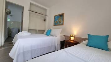 Quarto de hotel com duas camas, uma pequena mesa de cabeceira com abajur, um quadro na parede e um banheiro visível por uma porta aberta.