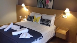 Una cama bien hecha con sábanas blancas, dos lámparas de pared y una mesita de noche con lámpara.
