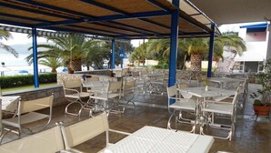 Un patio al aire libre con sillas y mesas de metal, palmeras y vista al mar.
