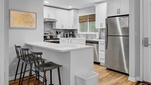 A modern kitchen with white cabinets, a stainless steel refrigerator, and a bar area with stools.