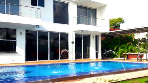 Een modern huis met twee verdiepingen, een zwembad, grote ramen en een overdekt terras.
