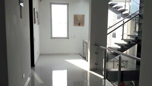 Een ruim, modern interieur met een lichte, zonnige hal die leidt naar een trap met glazen leuningen.