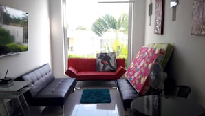 Een moderne woonkamer met een grijze bank, een rode bank, een zwarte eettafel en een aan de muur bevestigde televisie.