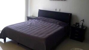 Een slaapkamer met een bed, nachtkastje en een kunstwerk aan de muur.