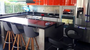 Een moderne keuken met een centraal eiland, een paar barkrukken, roestvrijstalen apparatuur en kastjes in rood en wit.