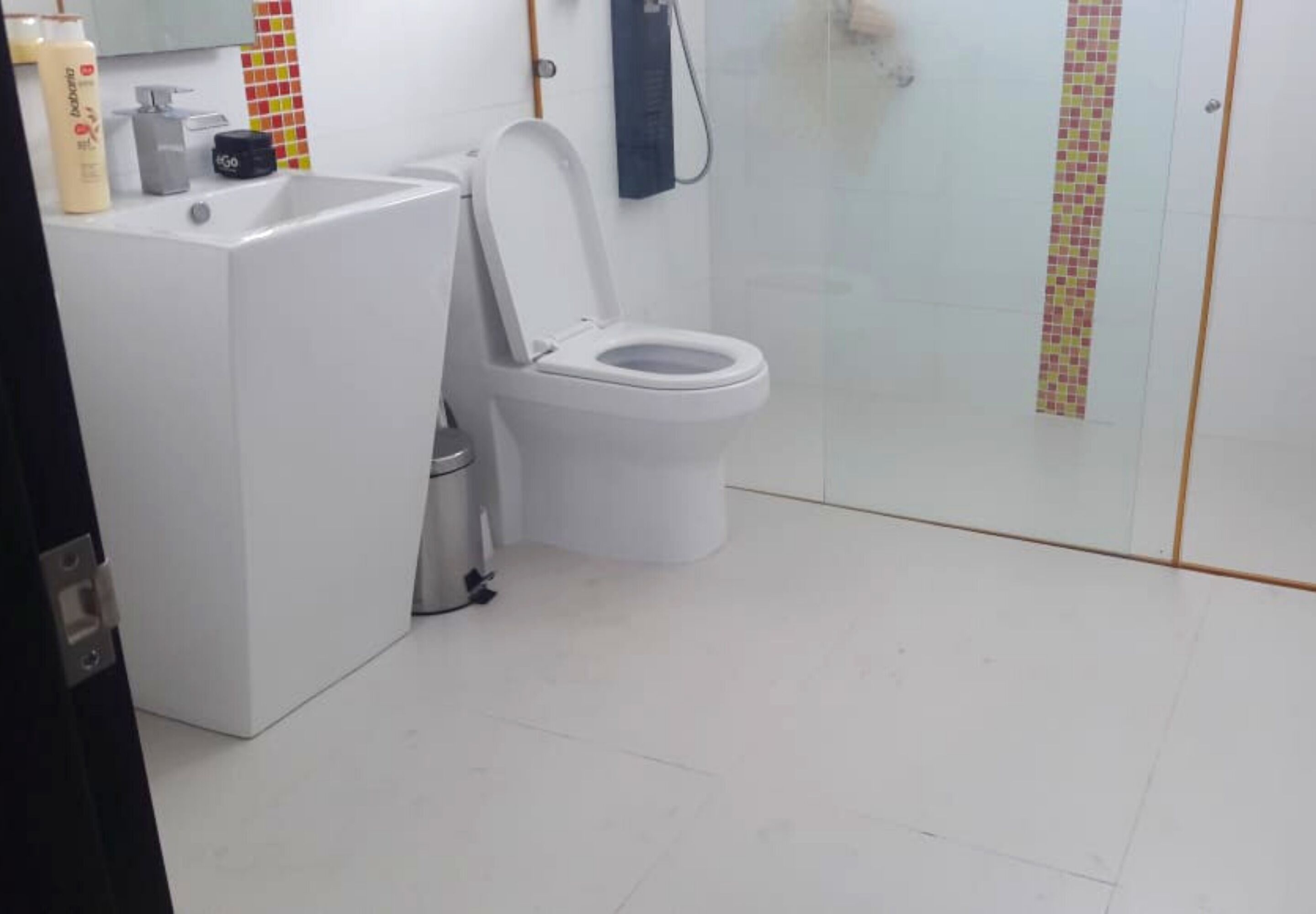 A bathroom with a white toilet, a sink, and a shower. There are toiletries on the sink.