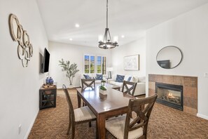 Un comedor con mesa de madera, sillas, una araña y una chimenea.