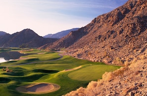 Un campo de golf con un lago, rodeado de montañas.