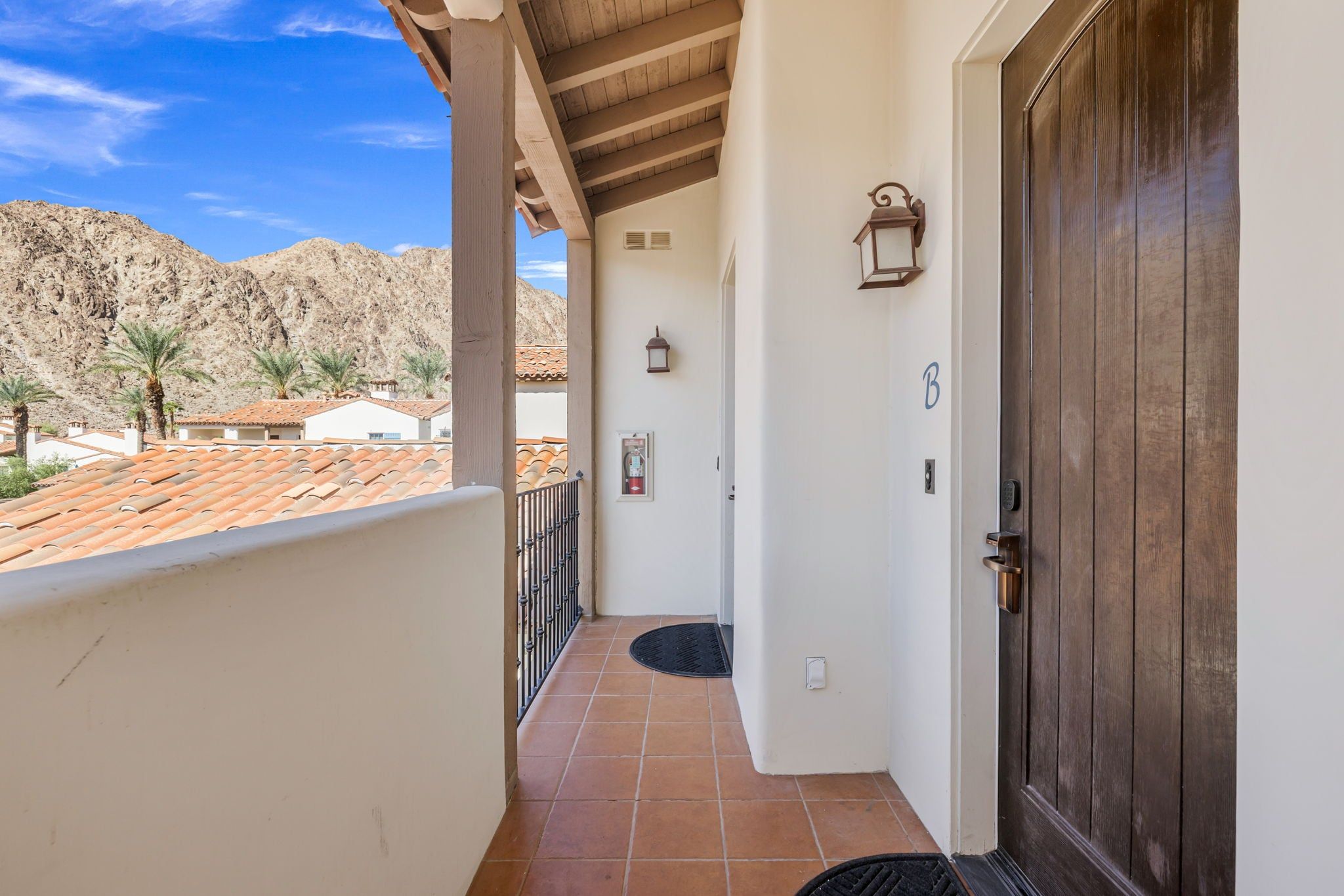 A balcony with a view of a mountainous landscape, a door with a number, and a small outdoor light fixture.