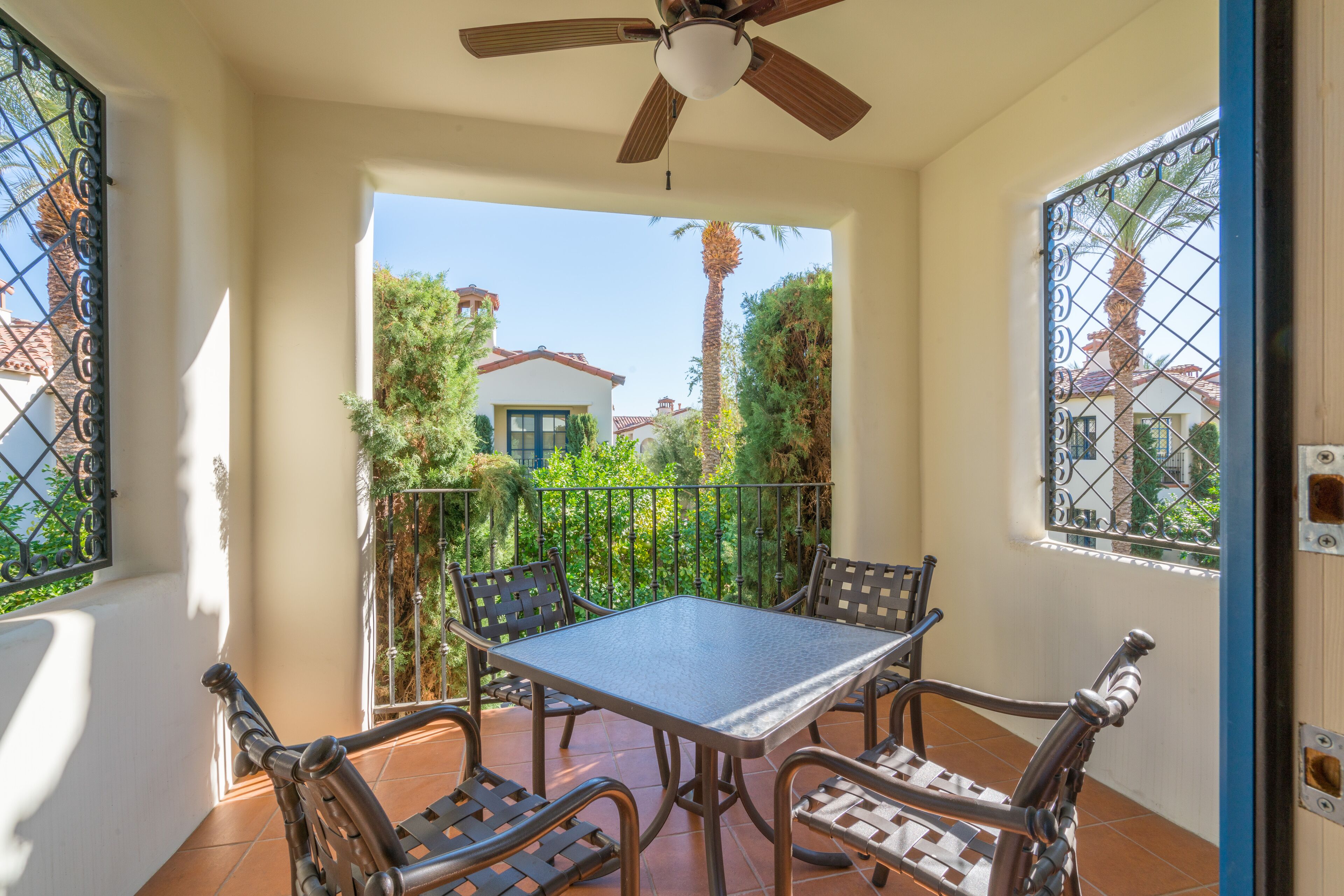 A balcony with a table and chairs, a ceiling fan, and a view of a house and palm trees.