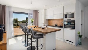 A modern kitchen with a central island, bar stools, and built-in appliances. - Luxury Villa Silvery with Pool (Kanica)