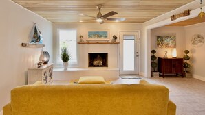 A living room with a fireplace, a ceiling fan, and a yellow sofa. - Luxury Beach House | Private Pool & Walk Everywhere (St. Pete Beach)