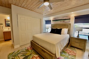 Une chambre à coucher comprenant un lit, une table de chevet, un ventilateur de plafond, une fenêtre avec vue et une porte.