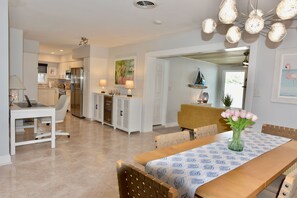 Une cuisine moderne avec des meubles blancs, un réfrigérateur en acier inoxydable et un coin repas comprenant une table et des chaises en bois.