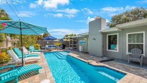 A backyard with a swimming pool, lounge chairs, and a covered patio area. - Luxury Beach House | Private Pool & Walk Everywhere (St. Pete Beach)