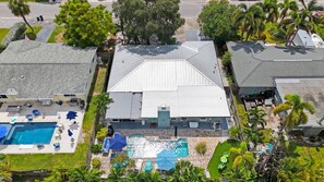 Vue a érienne d’une propriété résidentielle dotée d’une piscine, de meubles de patio et d’une grande maison avec un toit en pente.