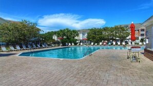 A swimming pool with lounge chairs and umbrellas, surrounded by buildings and trees. - 512 The Havens - Barefoot Resort Rentals (North Myrtle Beach)
