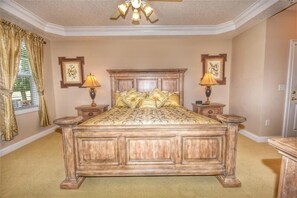 A bedroom with a large wooden bed, two bedside tables with lamps, a ceiling fan, and framed pictures on the walls.