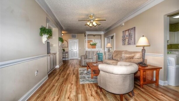 A spacious living area with a wooden floor, a ceiling fan, a sofa, a coffee table, and a lamp. - 512 The Havens - Barefoot Resort Rentals (North Myrtle Beach)