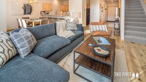 A modern living room with a grey sectional sofa, a wooden coffee table, and a staircase.