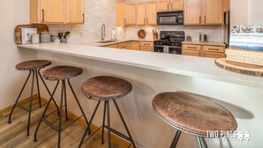 A modern kitchen with wooden cabinets, a stainless steel stove, and a bar area with stools.