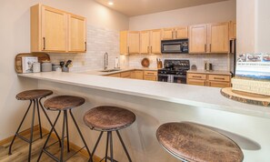 Une cuisine moderne avec des meubles en bois, une cuisinière en acier inoxydable et un coin bar avec des tabourets.